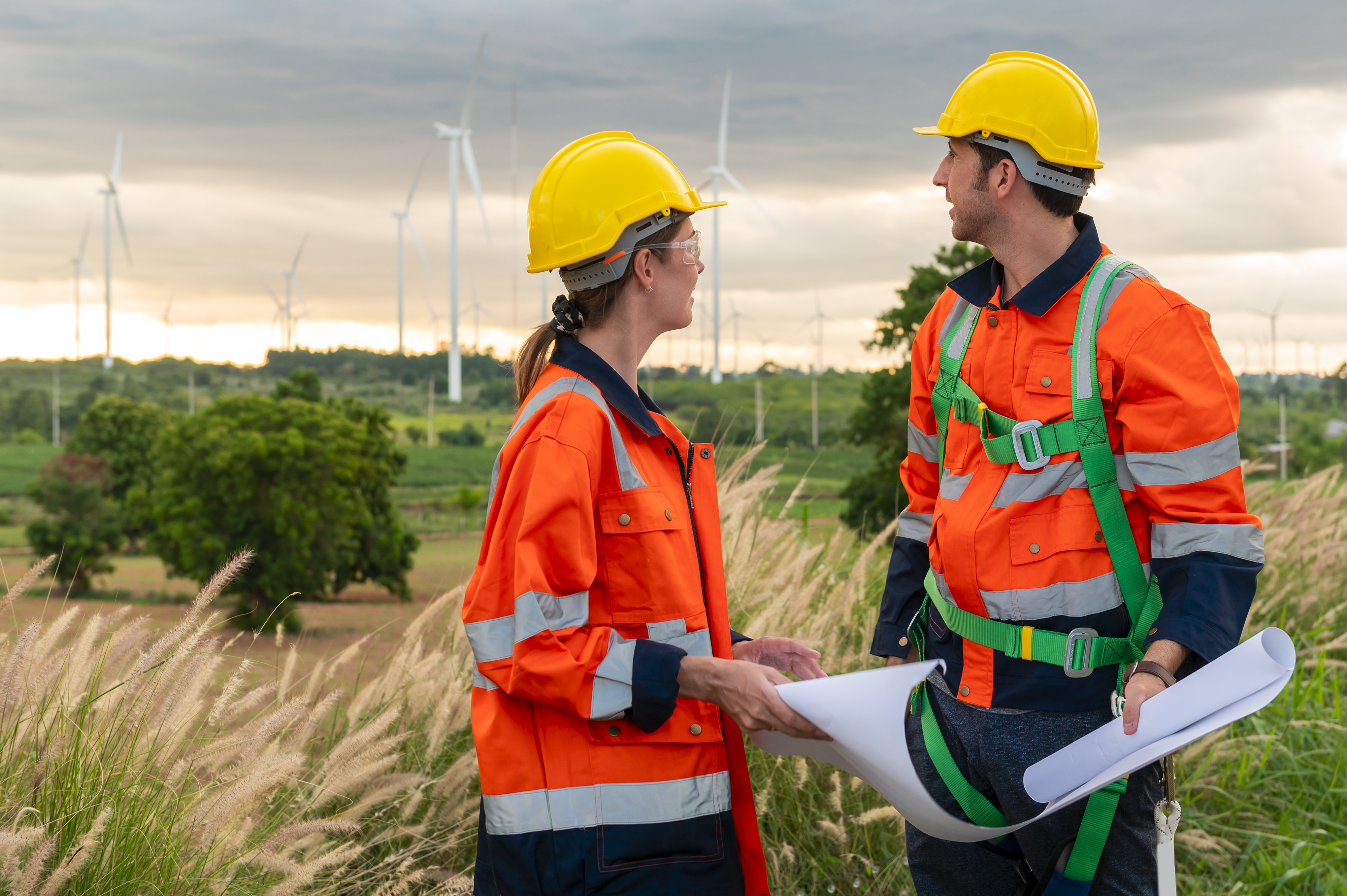 Smart engineer with protective helmet holding the blueprint working at electrical turbines field